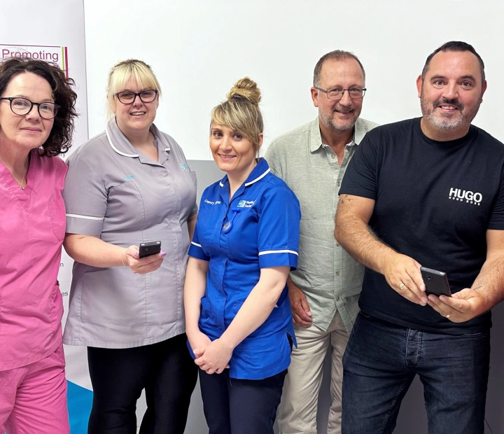 Pět usmívajících se lidí stojí společně ve zdravotnickém oděvu, přičemž dva z nich drží překladač.