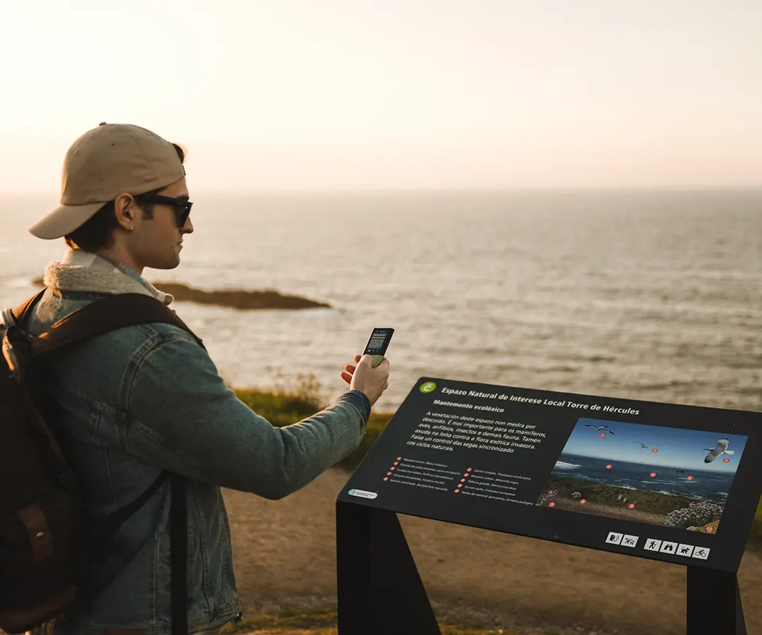 a man at the beautiful seaside using a photo translator to read a sign with tourist information about his location